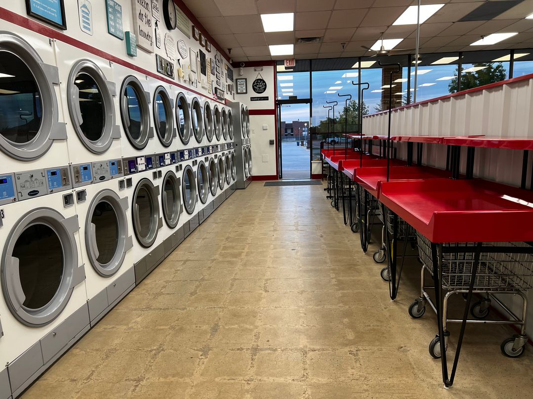 Rows of dryers and red folding tables inside Laura's Laundromat